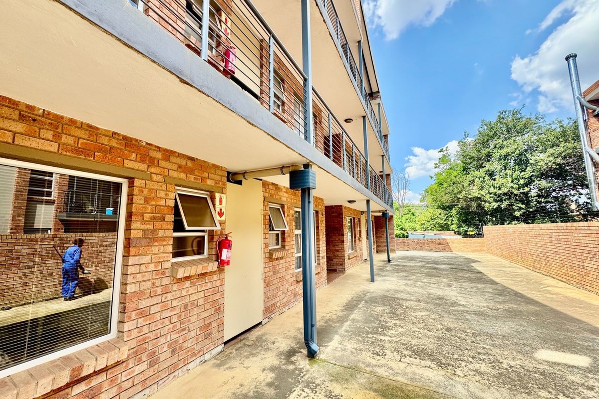 Rear exterior view of a multi-story apartment building featuring face brick construction, metal balcony railings, and paved ground level area.
