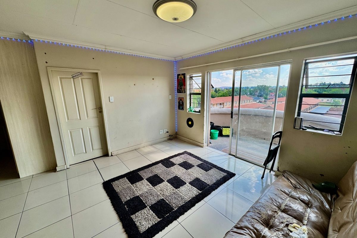 A living room featuring tiled flooring, a sliding glass door leading to a balcony, and large windows providing natural light and neighborhood views.