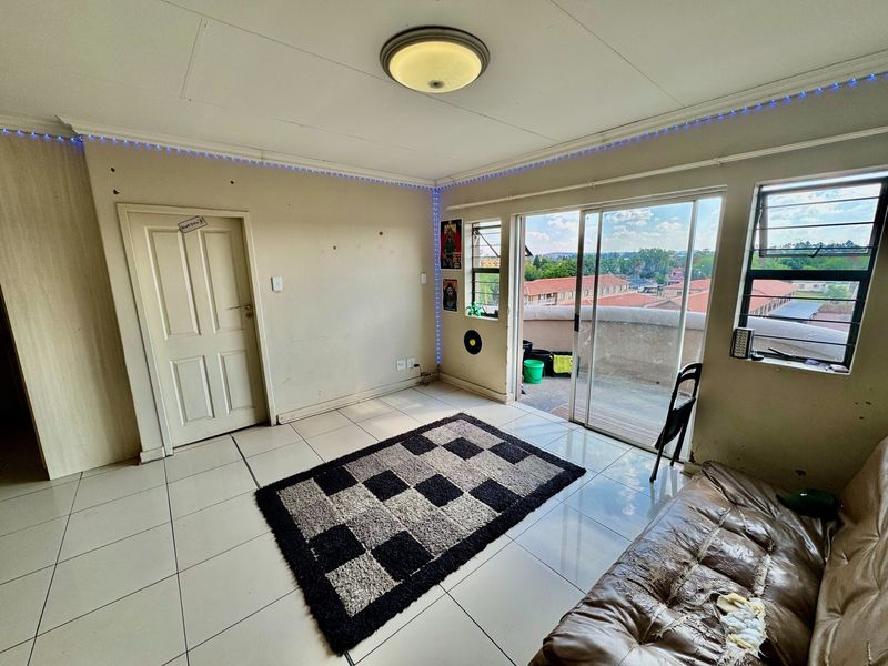 A living room featuring tiled flooring, a sliding glass door leading to a balcony, and large windows providing natural light and neighborhood views.