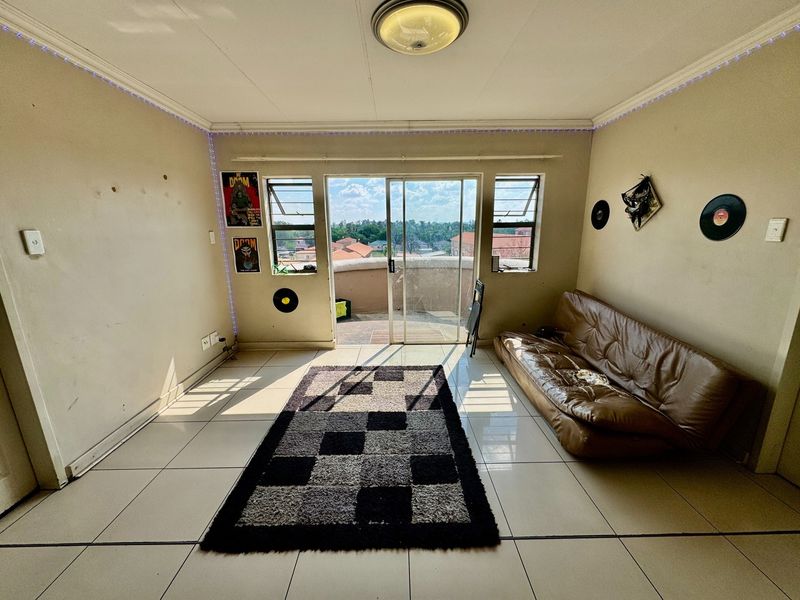 A living room featuring tiled floors, louver windows, and a sliding glass door leading to a balcony, offering natural light and outdoor access.