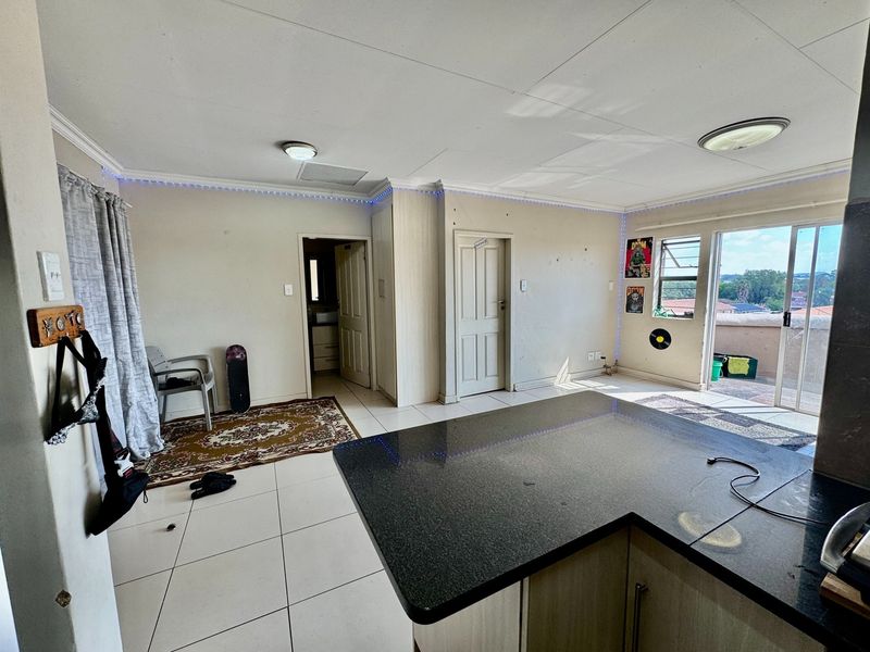 Open plan living area featuring tiled floors, granite kitchen countertops, and sliding door access to a balcony with natural light.