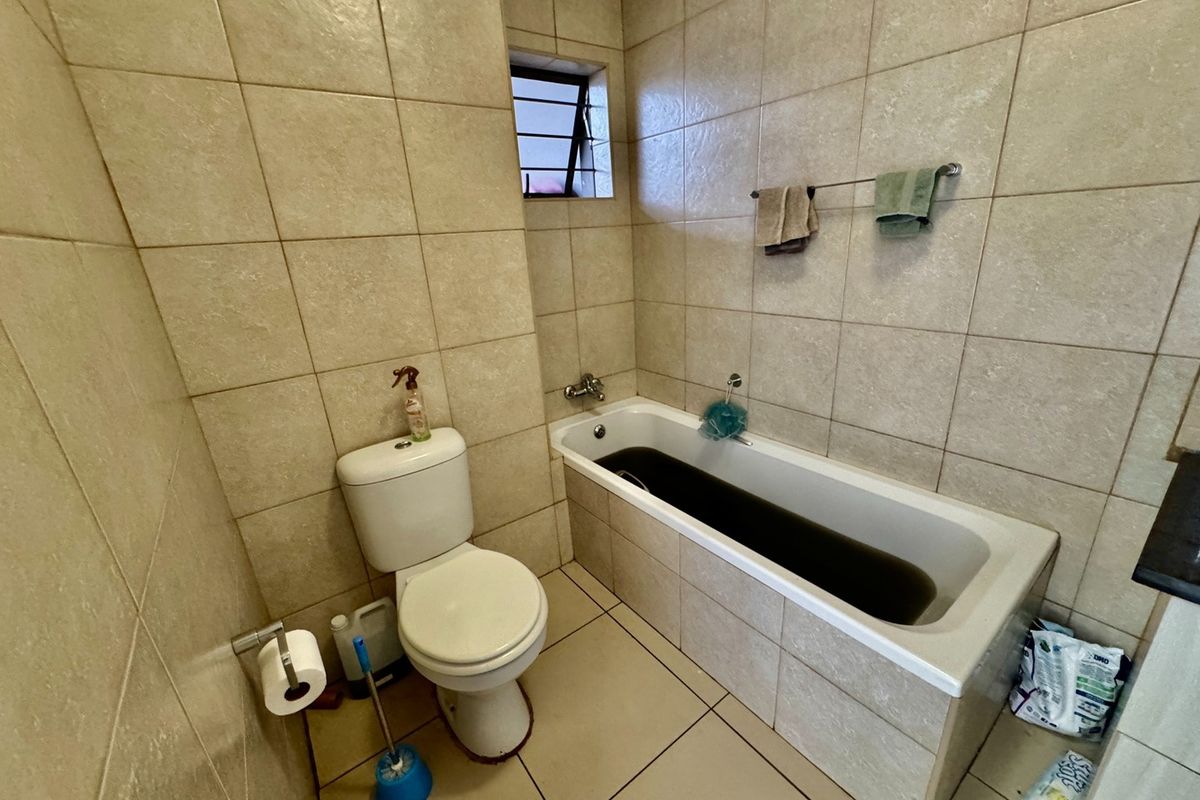 A functional bathroom featuring full-height wall tiling, a standard bathtub, and a toilet, with a small louver window for ventilation.