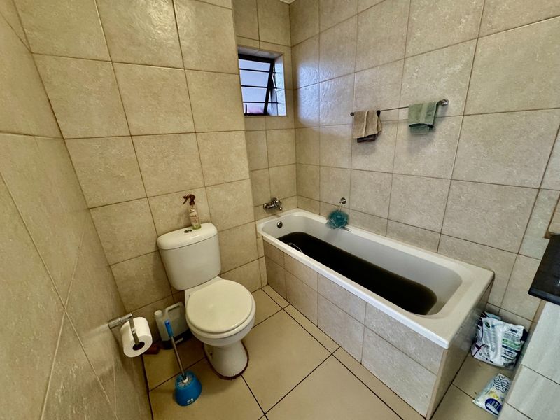 A functional bathroom featuring full-height wall tiling, a standard bathtub, and a toilet, with a small louver window for ventilation.