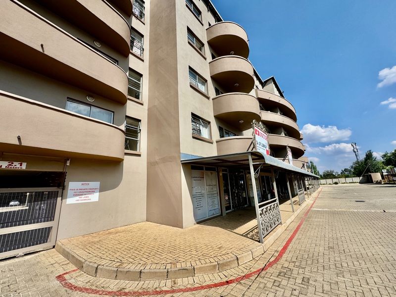 Exterior view of a multi-story apartment building featuring curved balconies, a paved driveway, and a covered entrance area with signage.