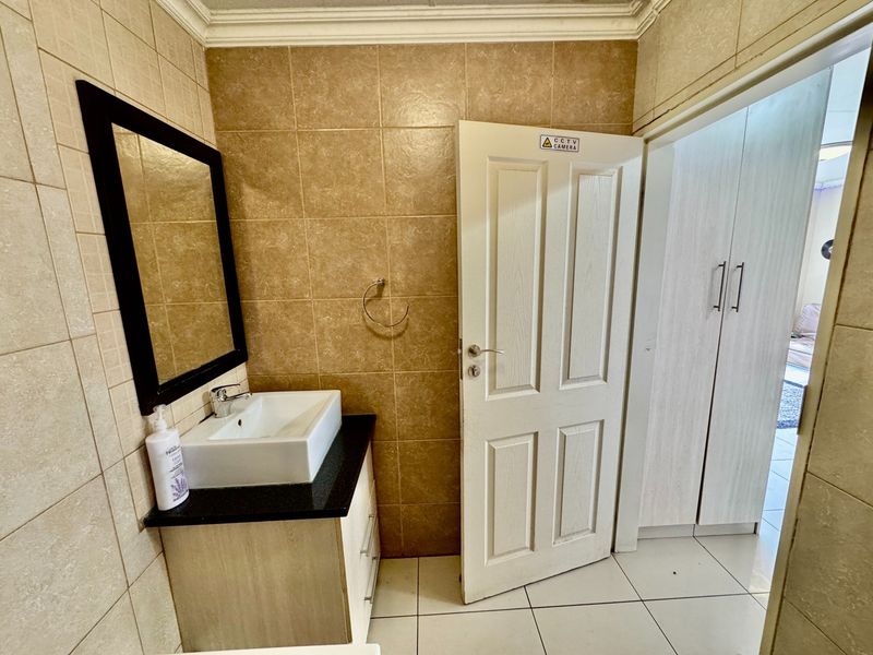 A functional bathroom featuring a vessel sink on a vanity cabinet, wall-mounted mirror, and built-in storage cupboards with neutral tiled finishes.