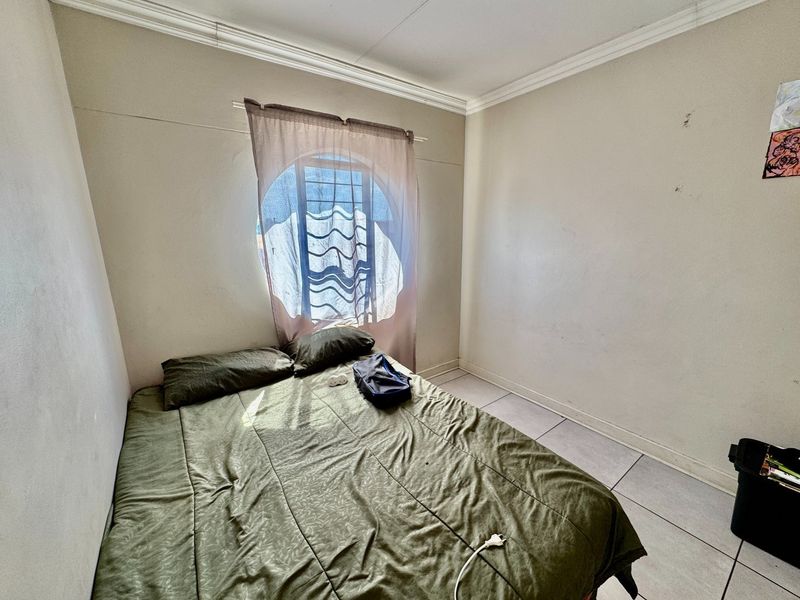 A bedroom featuring tiled flooring, a circular window with security bars, and crown molding. The space requires cosmetic wall repairs and fresh paint.
