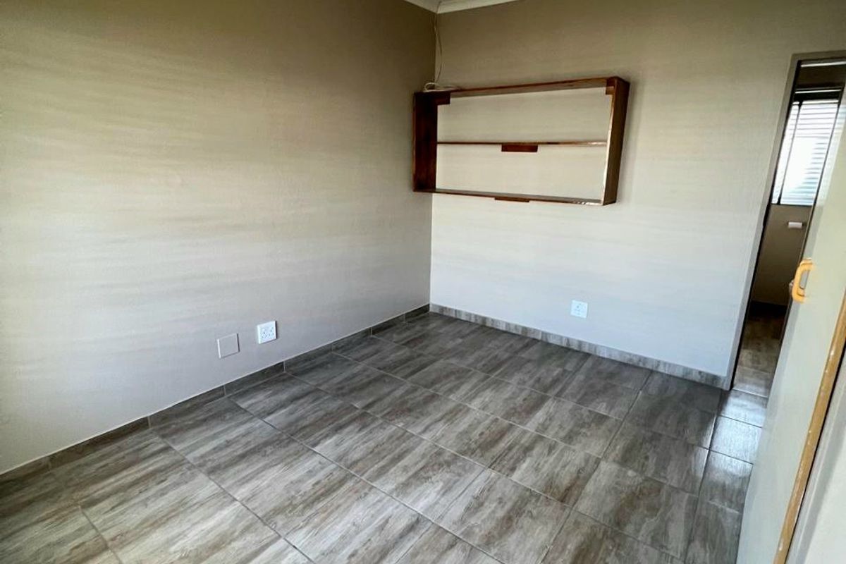 An empty bedroom featuring wood-look tiled flooring, neutral wall paint, and a built-in wall shelf unit.