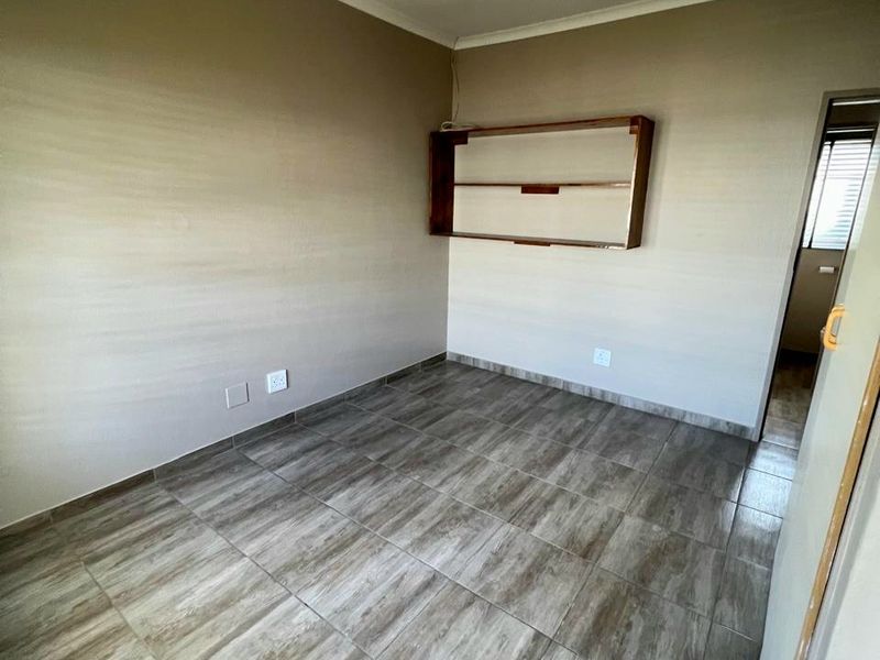 An empty bedroom featuring wood-look tiled flooring, neutral wall paint, and a built-in wall shelf unit.