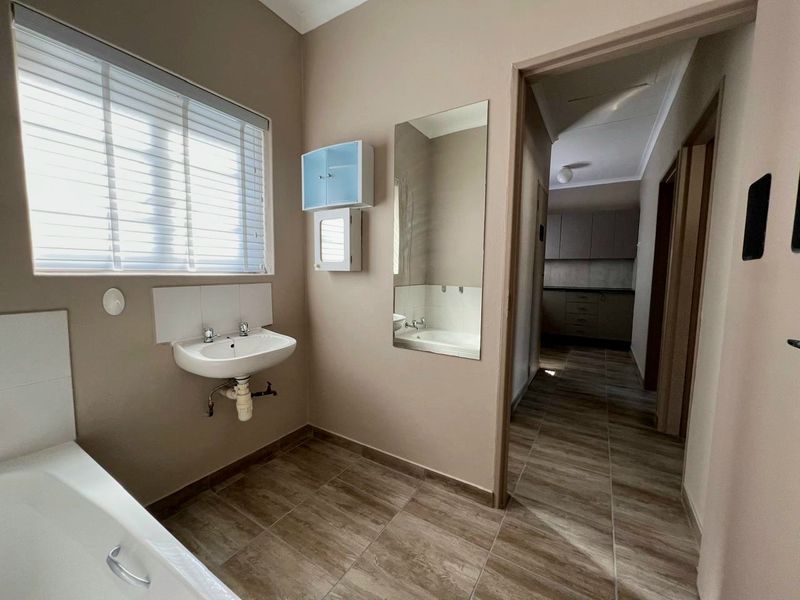 A functional bathroom featuring a bathtub, wall-mounted basin, and tiled flooring, with a view leading into the adjacent kitchen area.