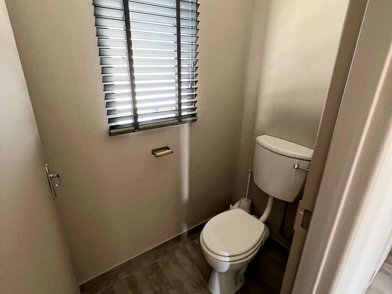 A compact, clean guest toilet featuring neutral wall tones, tiled flooring, and a window with fitted venetian blinds.
