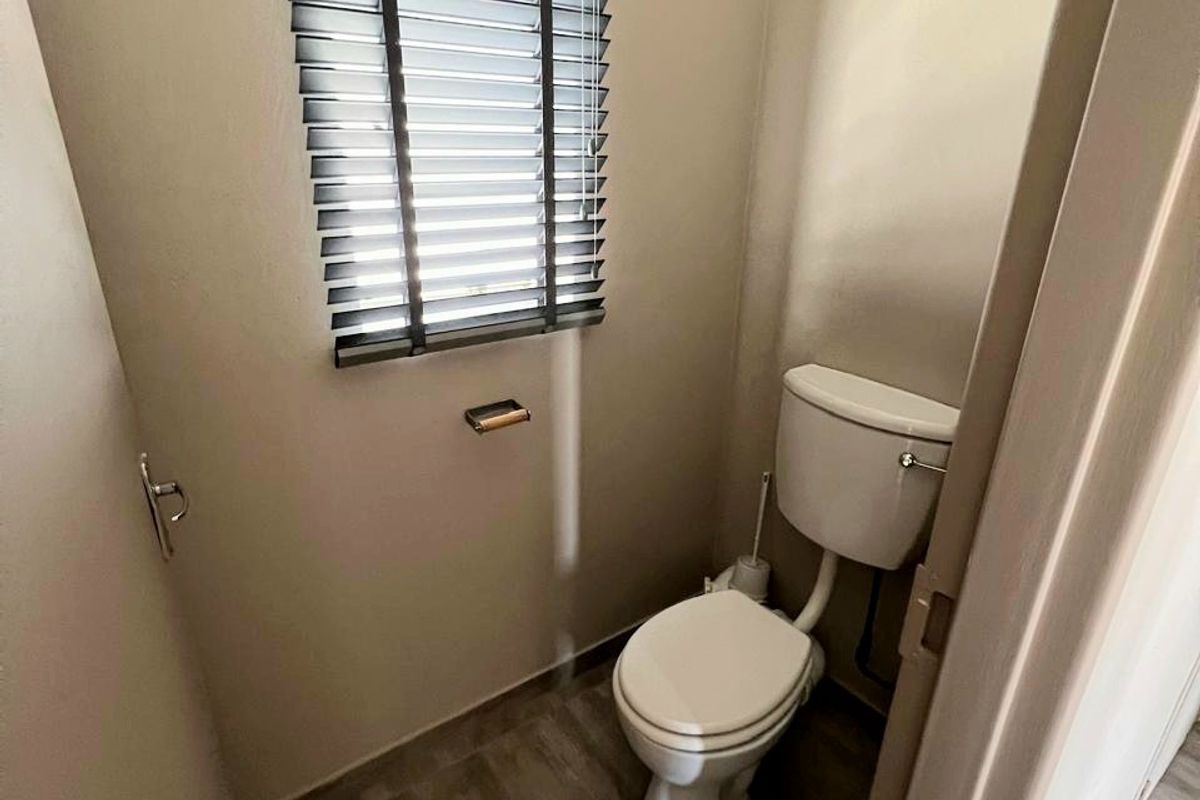 A compact, clean guest toilet featuring neutral wall tones, tiled flooring, and a window with fitted venetian blinds.