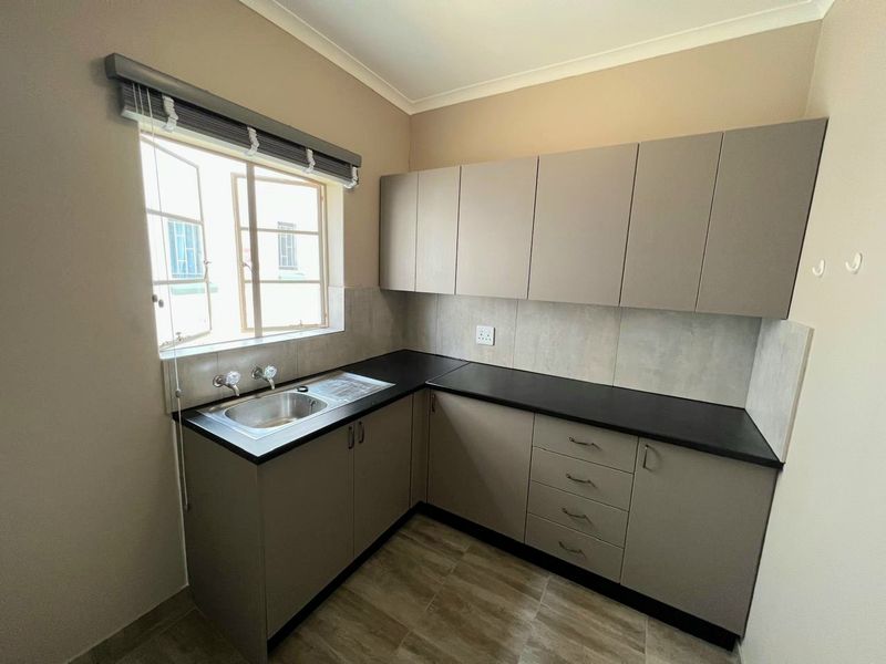A clean and functional kitchen featuring modern laminate cabinetry, dark countertops, a stainless steel sink, and neutral tiled finishes.