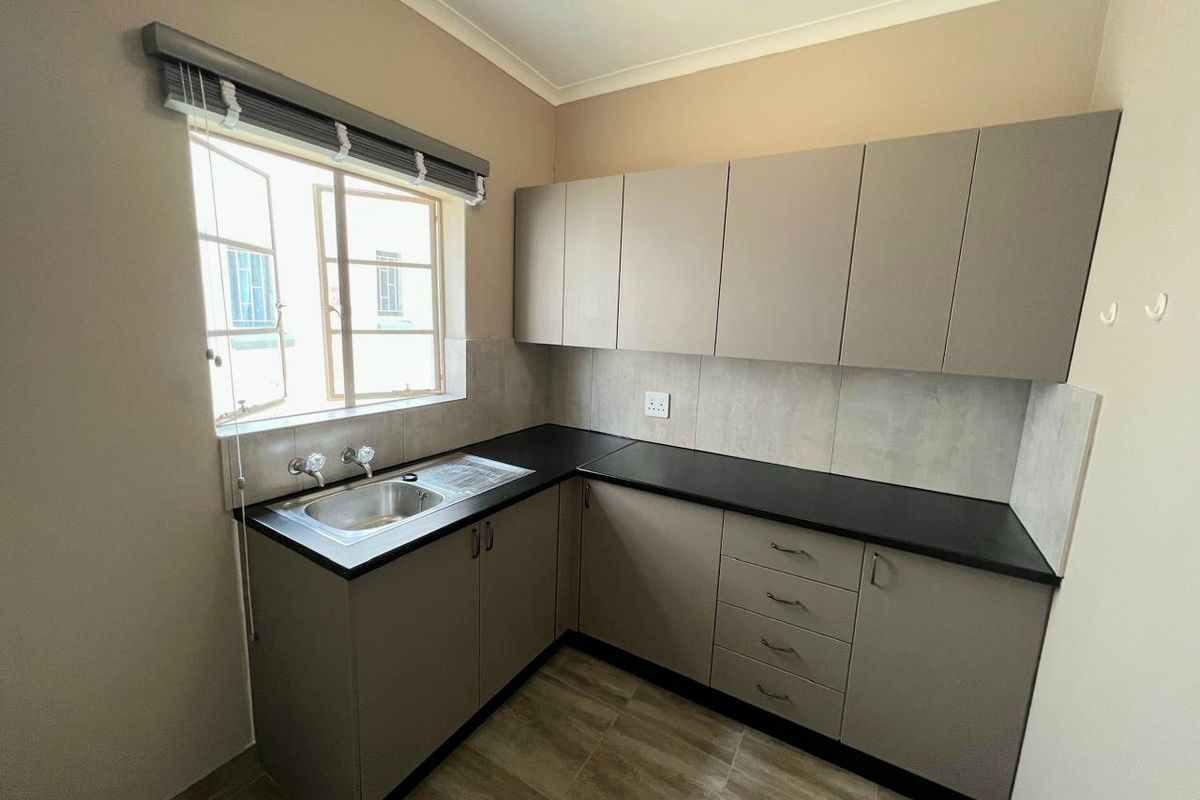 A clean and functional kitchen featuring modern laminate cabinetry, dark countertops, a stainless steel sink, and neutral tiled finishes.