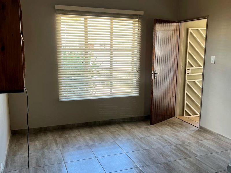 A bright, empty bedroom featuring neutral wall tones, tiled flooring, and a window fitted with venetian blinds.