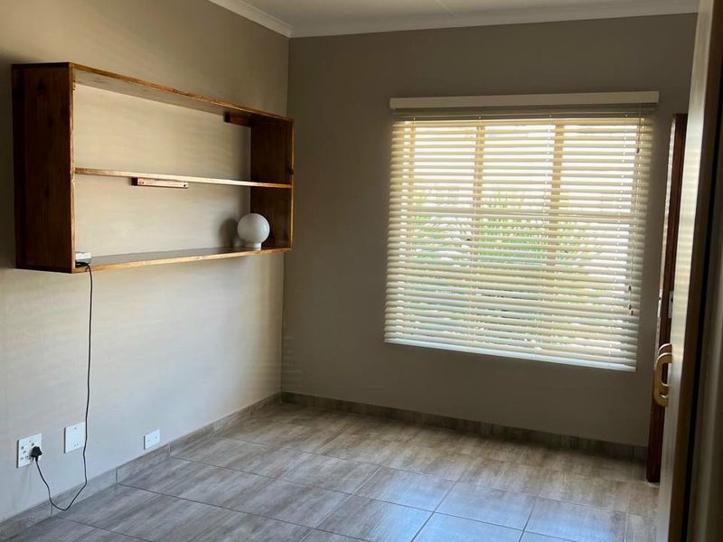 A clean, empty bedroom featuring neutral wall tones, durable tiled flooring, built-in wall shelving, and venetian blinds for adjustable natural light.