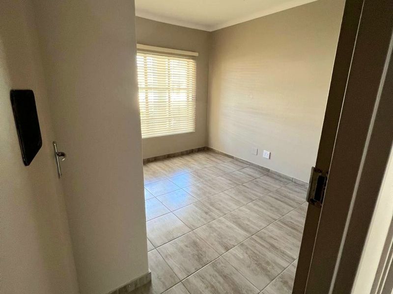 A bright, empty bedroom featuring neutral wall tones, tiled flooring, and fitted venetian blinds, offering a clean and versatile space.