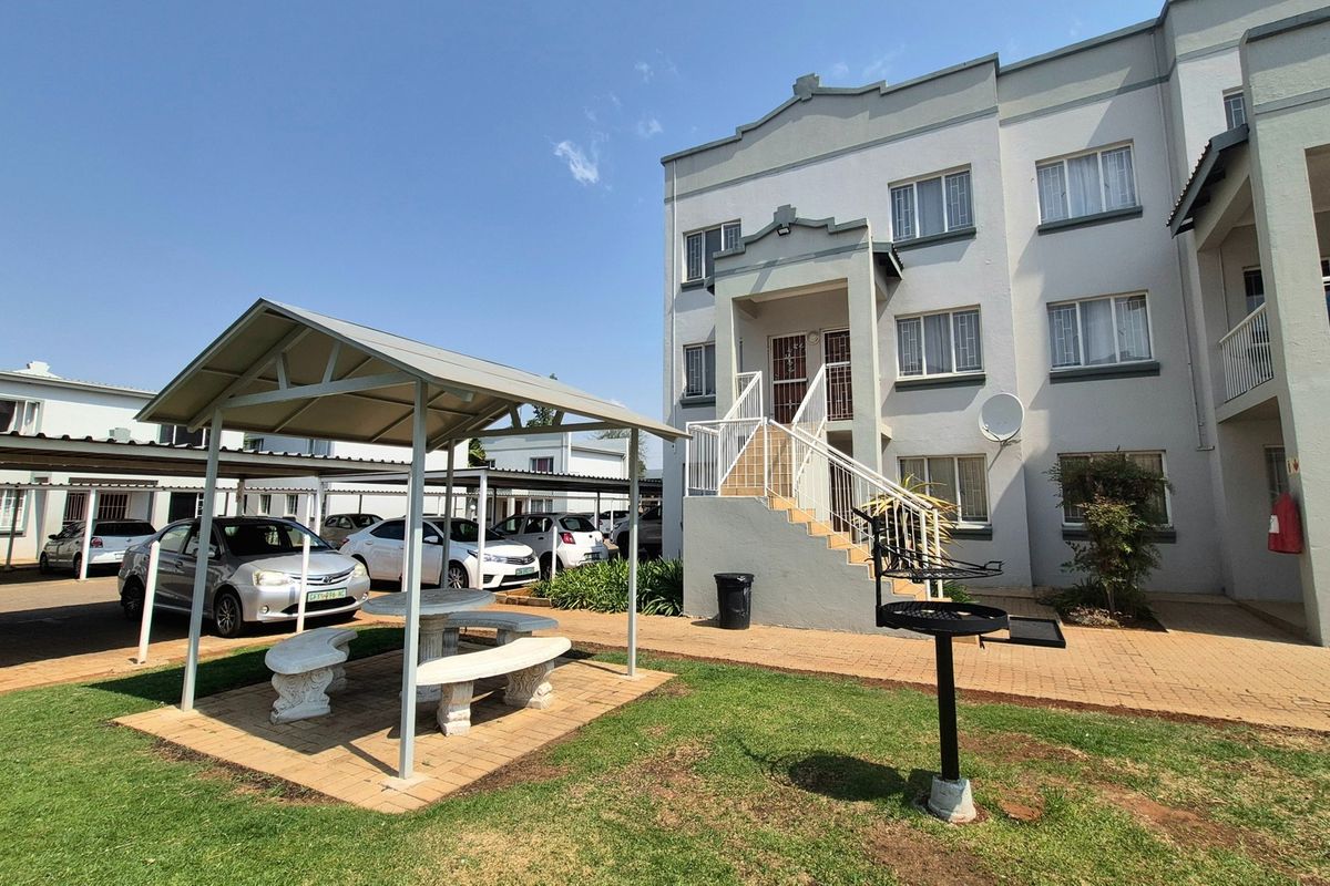 Exterior view of an apartment complex featuring a paved courtyard, a covered gazebo seating area, and a built-in braai facility.