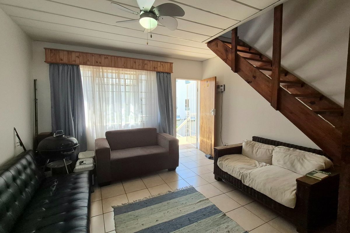 Open-plan living area featuring tiled flooring, a ceiling fan, and a wooden staircase leading to the upper level.