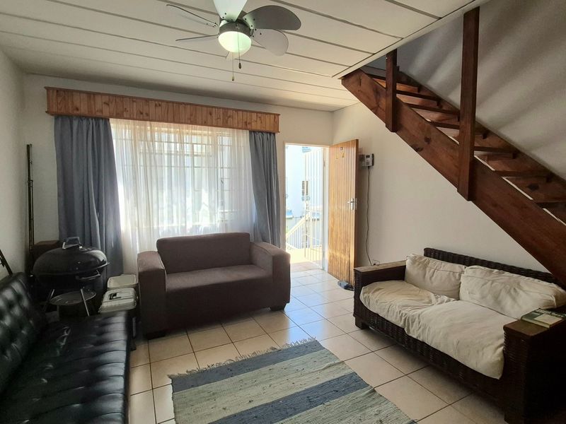 Open-plan living area featuring tiled flooring, a ceiling fan, and a wooden staircase leading to the upper level.