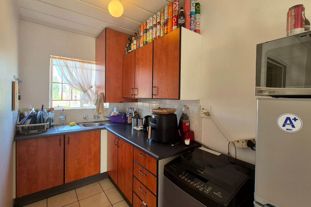 A compact kitchen featuring wood-look cabinetry, laminate countertops, a stainless steel sink, and tiled backsplash, offering a functional layout for an apartment.