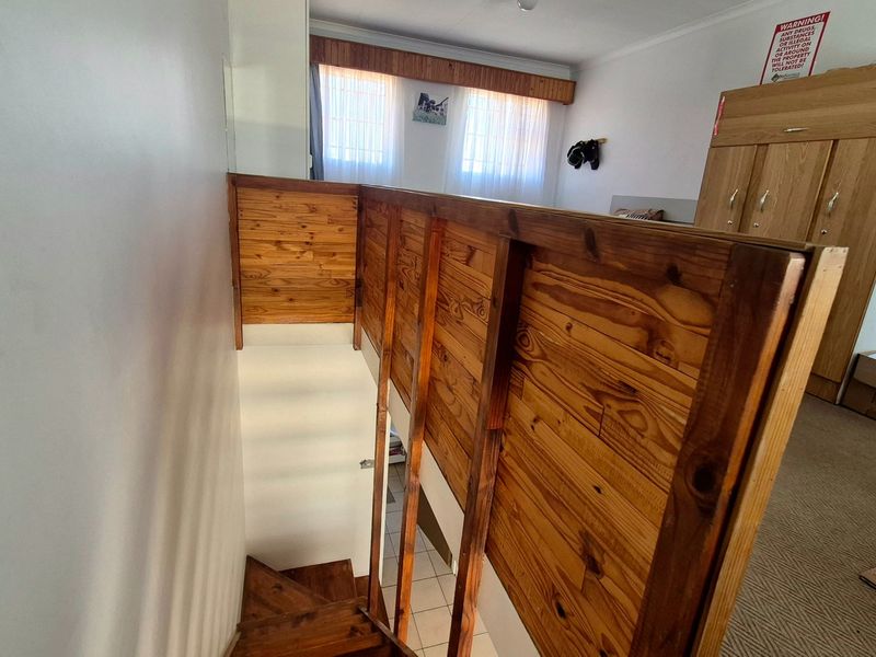A view of an upper-level landing area featuring a wooden staircase and balustrade, leading down to the lower level of the apartment.