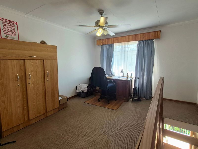A bedroom featuring a ceiling fan, built-in wardrobe, and wooden balustrade overlooking the staircase, with carpeted flooring throughout.