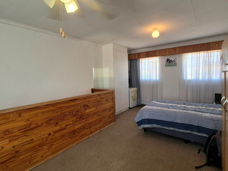 A bedroom featuring built-in cupboards, timber wall paneling, and a ceiling fan, offering a functional space with potential for modern updates.