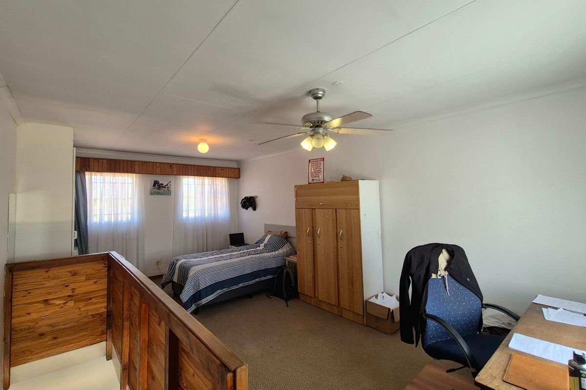 A spacious bedroom featuring carpeted flooring, a ceiling fan, and a timber balustrade overlooking the lower level.