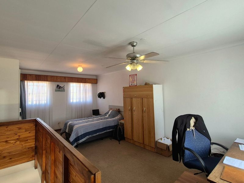A spacious bedroom featuring carpeted flooring, a ceiling fan, and a timber balustrade overlooking the lower level.