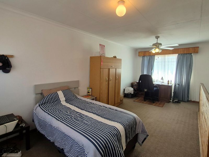 Spacious bedroom featuring carpeted flooring, a ceiling fan, and a wooden window pelmet, offering a functional layout with ample natural light.