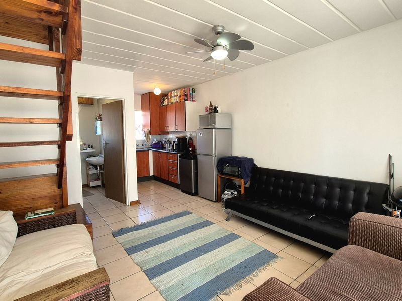 Open plan living area featuring a wooden staircase, tiled flooring, and a compact kitchen with built-in cabinetry.