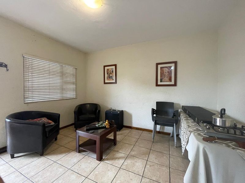 A living room area featuring tiled flooring and venetian blinds, currently showing signs of wear on the walls.