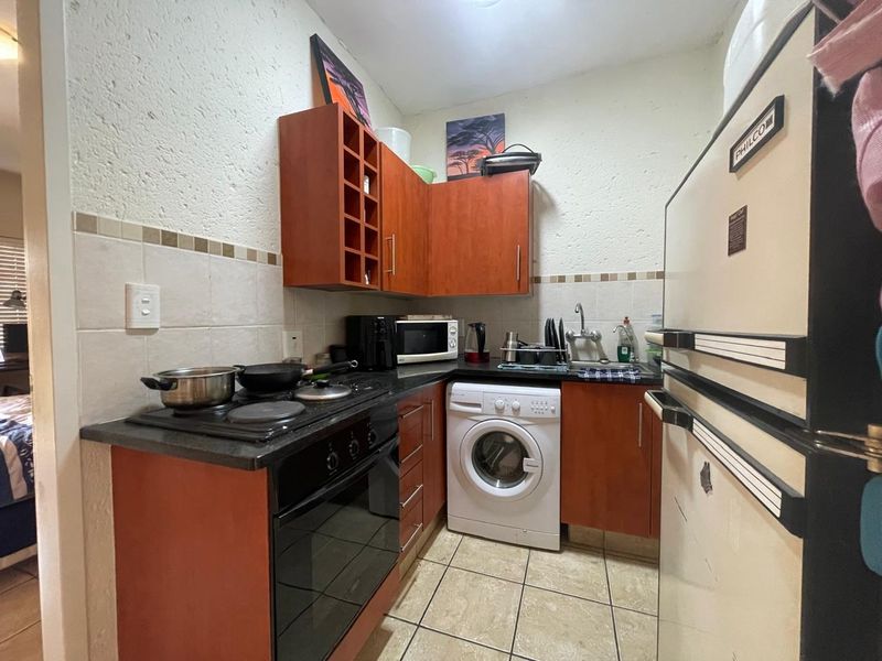 Compact kitchen featuring wooden cabinetry, laminate countertops, built-in electric stove and oven, tiled backsplash, and an integrated washing machine.