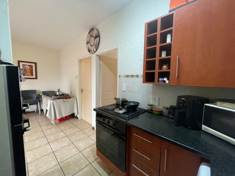 A functional kitchen featuring built-in wooden cabinetry, granite countertops, an integrated electric hob and oven, and tiled flooring.