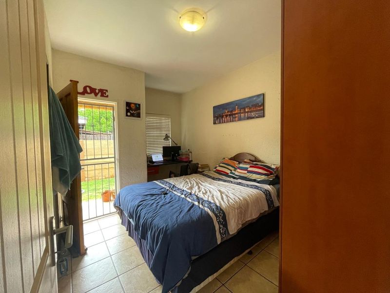 A functional bedroom featuring tiled flooring, a ceiling light fixture, and direct access to an outdoor area through a security gate.
