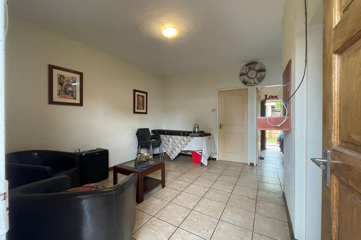 A living area featuring tiled flooring and access to an adjoining room, showing signs of wear on the walls.