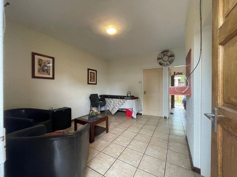 A living area featuring tiled flooring and access to an adjoining room, showing signs of wear on the walls.