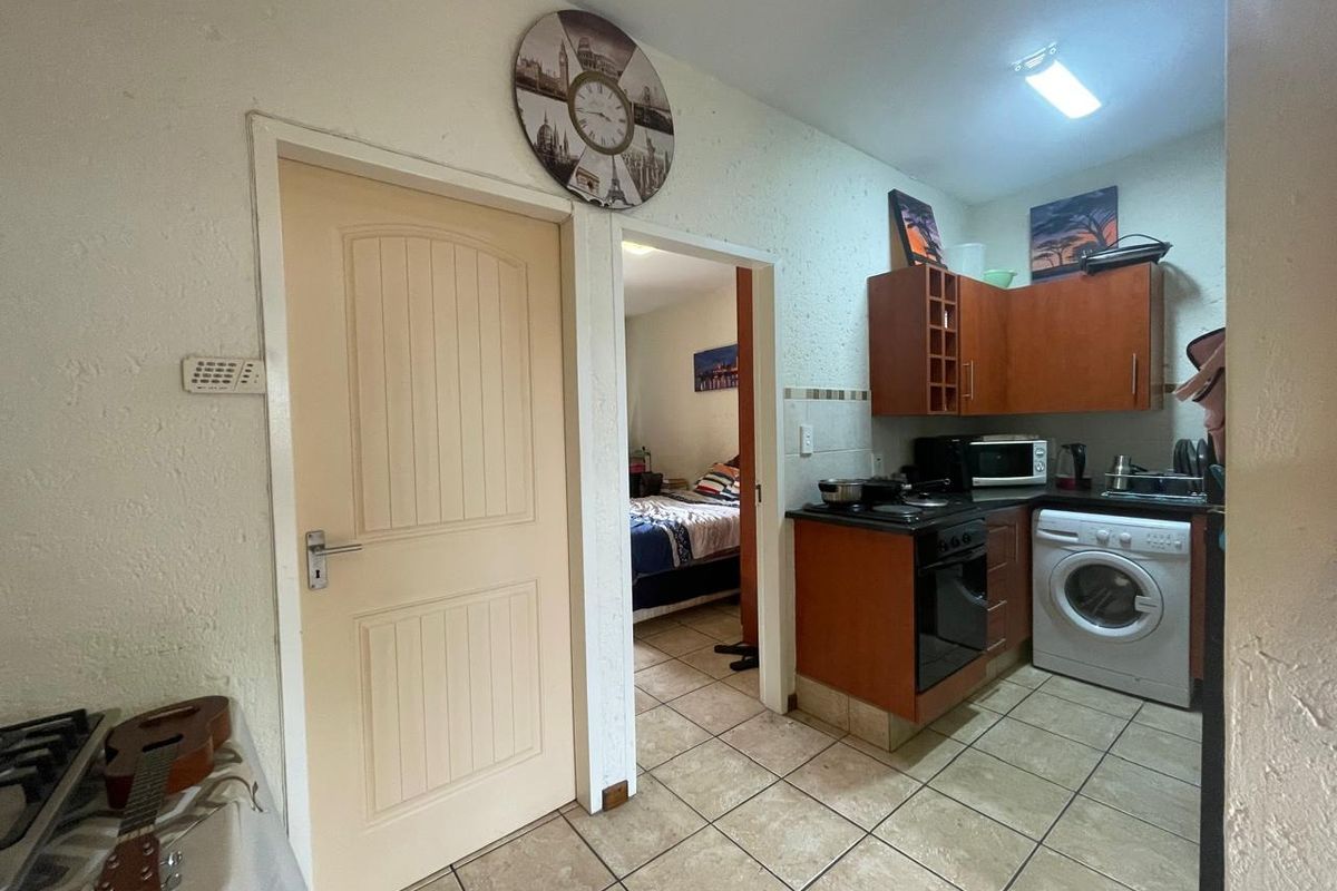 Compact kitchen featuring built-in wooden cabinetry, electric oven and hob, tiled flooring, and a tiled backsplash, with direct access to an adjacent bedroom.