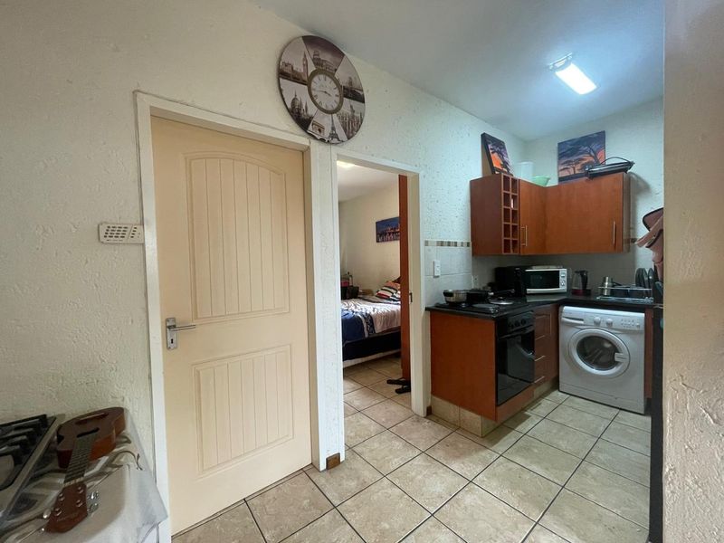Compact kitchen featuring built-in wooden cabinetry, electric oven and hob, tiled flooring, and a tiled backsplash, with direct access to an adjacent bedroom.