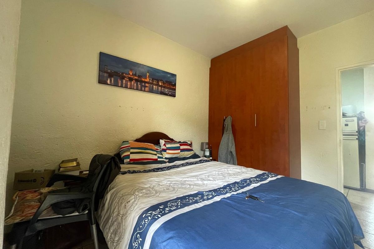 A functional bedroom featuring a built-in wooden wardrobe and tiled flooring, offering a practical layout with potential for cosmetic updates.