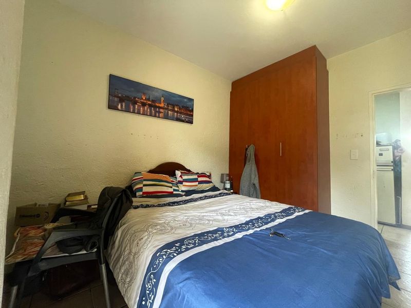 A functional bedroom featuring a built-in wooden wardrobe and tiled flooring, offering a practical layout with potential for cosmetic updates.