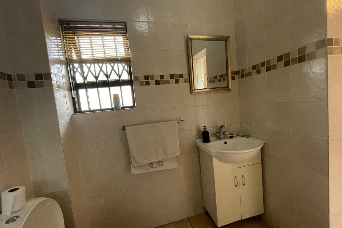 A functional bathroom featuring tiled walls with decorative accents, a vanity cabinet with a basin, and a window with security bars.