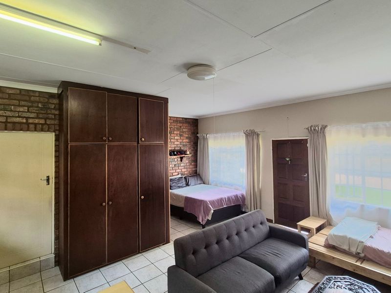 Spacious bedroom featuring exposed brick walls, built-in wooden cupboards, and tiled flooring, offering a functional layout with natural light.