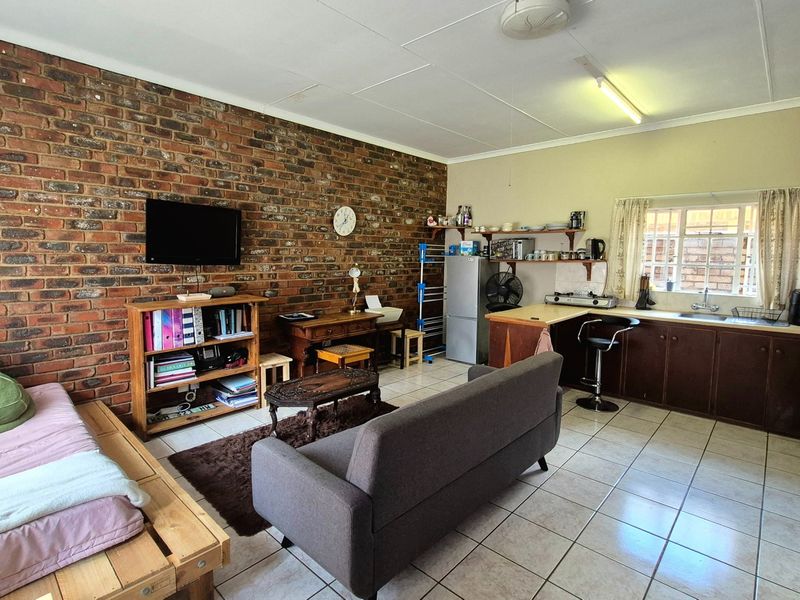 Open-plan living and kitchen area featuring an exposed brick feature wall, ceramic tiled flooring, and functional built-in kitchen cabinetry.