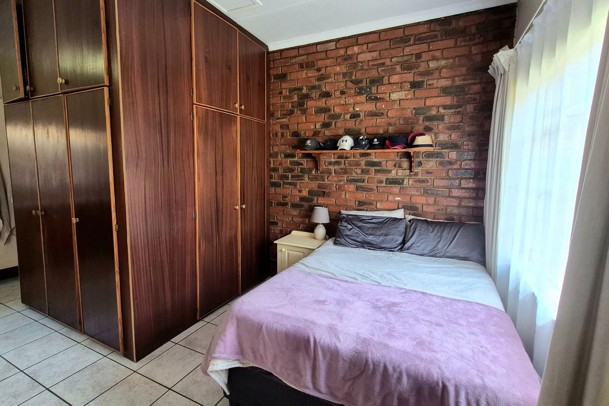 Bedroom featuring built-in wooden cupboards, an exposed brick feature wall, and tiled flooring, offering a functional and classic layout.