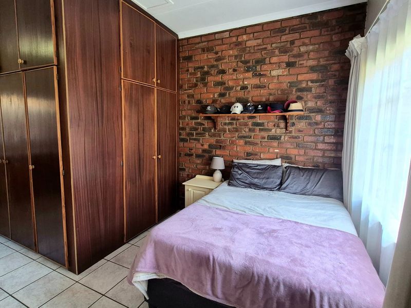 Bedroom featuring built-in wooden cupboards, an exposed brick feature wall, and tiled flooring, offering a functional and classic layout.