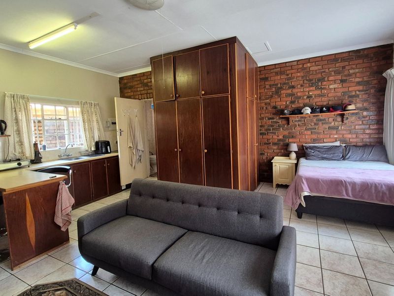 Open-plan studio apartment featuring a kitchenette with built-in cabinetry, exposed brick wall, and tiled flooring throughout.