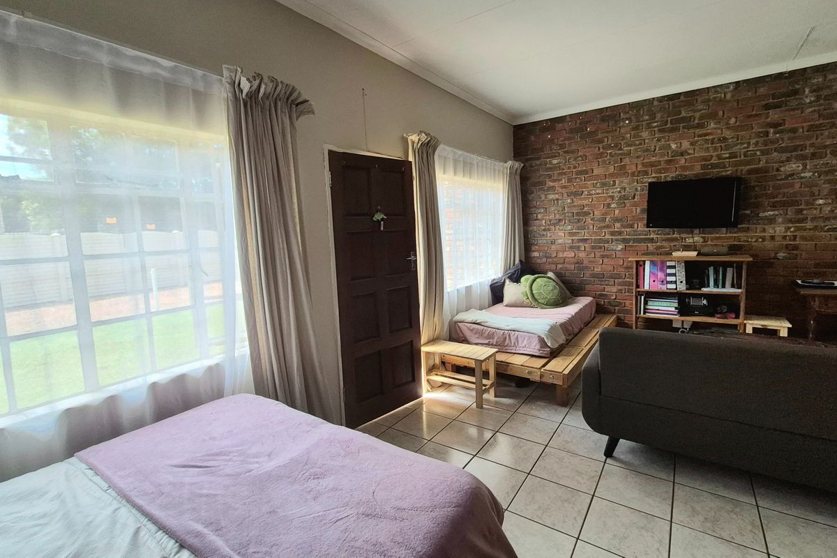 A living area featuring an exposed brick wall, ceramic tiled flooring, and large windows providing natural light.