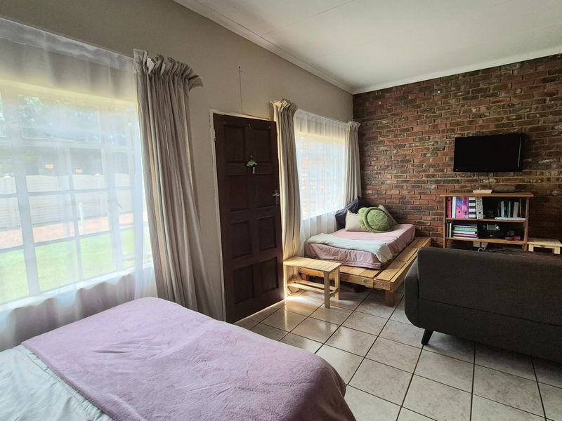 A living area featuring an exposed brick wall, ceramic tiled flooring, and large windows providing natural light.