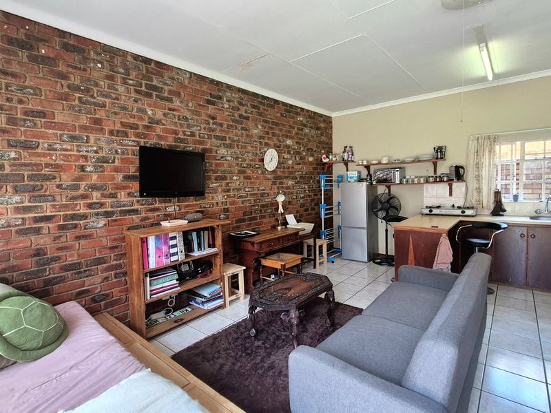 Open-plan living area featuring an exposed brick feature wall, tiled flooring, and a functional kitchen with built-in cabinetry and sink.